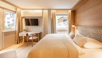 Gemütliches Schlafzimmer mit großem Bett, Fenster, Schreibtisch und Fernseher