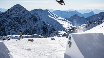 Snowboarder macht einen Sprung im Stubai Gletscher Park vor Bergkulisse