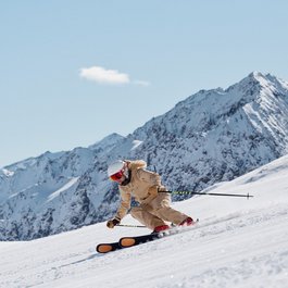 Frau in beige Skianzug beim Skifahren vor schneebedeckten Bergen