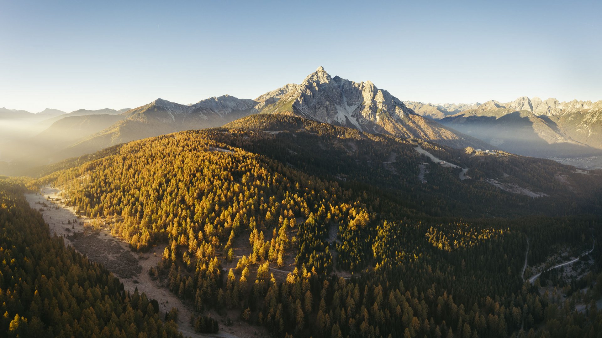 Autumn view of forested mountain with sunlit peak and clear sky
