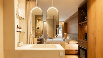 Modernes Hotelzimmer mit Waschbecken, beleuchteten Spiegeln und Holzmöbeln