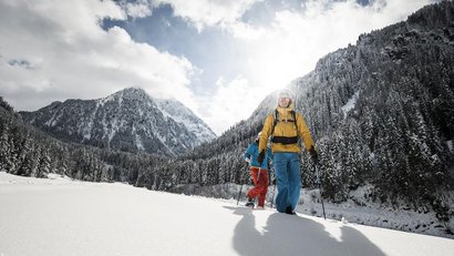 Two people snowshoeing through a snowy mountain landscape in sunlight