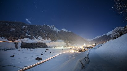 Schneebedecktes Bergdorf bei Nacht mit Sternenhimmel und beleuchteten Häusern