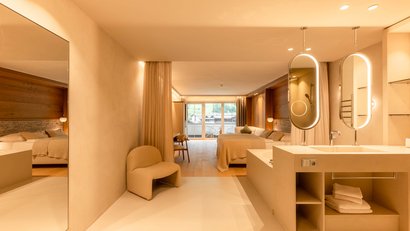 Modernes Hotelzimmer mit Doppelbett, Sessel, Balkon und begehbarem Waschbereich